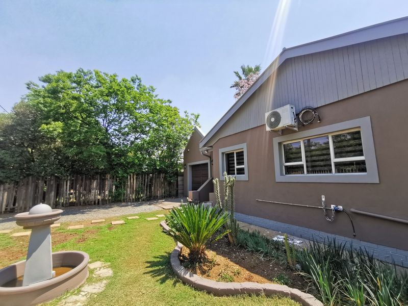 Rear exterior view of the house featuring a landscaped garden, a decorative fountain, and a paved driveway area.