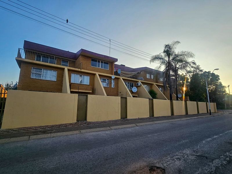 Street view of a multi-story apartment complex featuring brick facade, private balconies, and a secure perimeter wall.