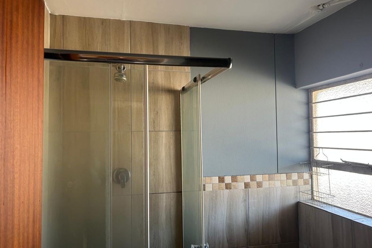 A functional bathroom featuring a glass shower enclosure with wood-look wall tiling and a window with security bars.