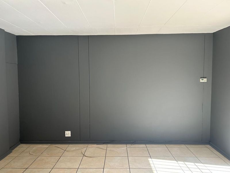An empty living area featuring dark grey painted walls, neutral floor tiles, and a wall-mounted security alarm keypad.