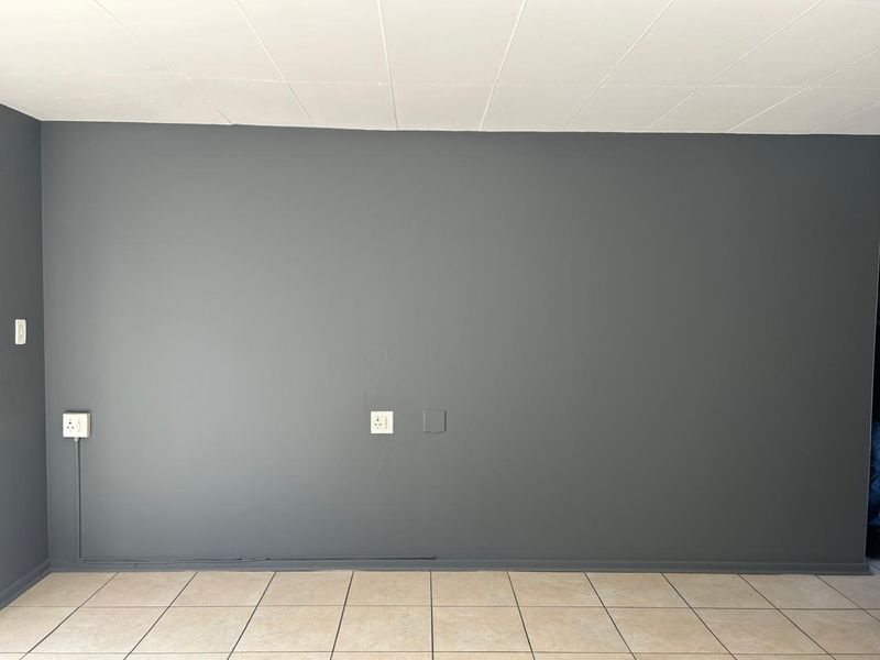 An empty living area featuring dark grey painted walls, neutral tiled flooring, and visible electrical power points.