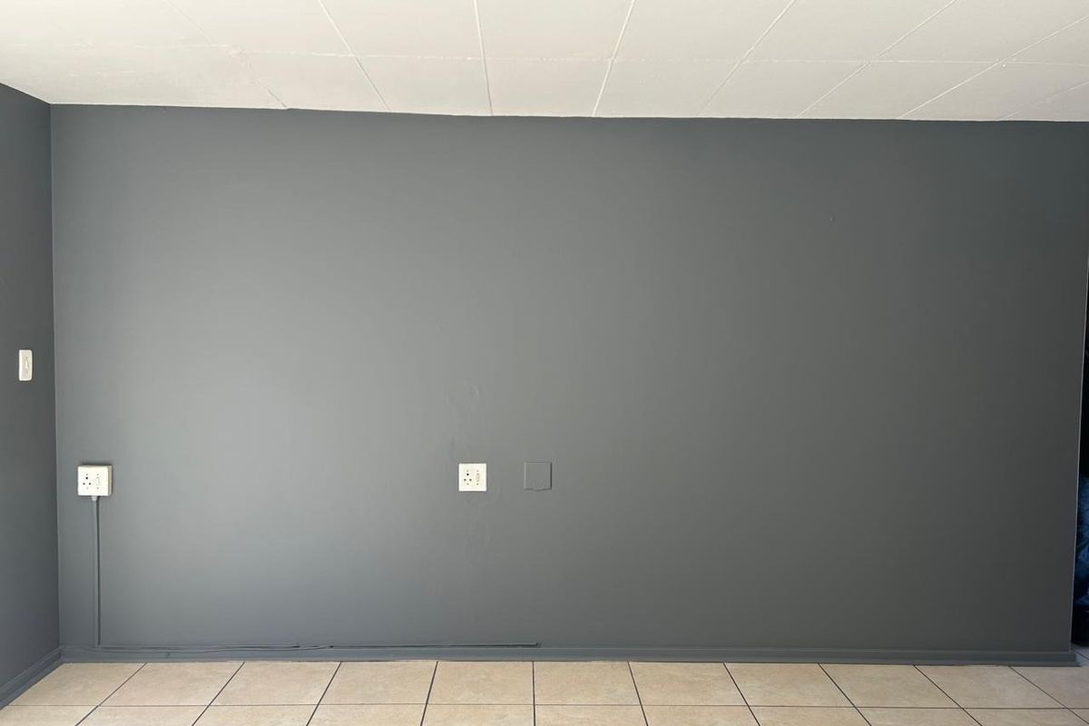 An empty living area featuring dark grey painted walls, neutral tiled flooring, and visible electrical power points.