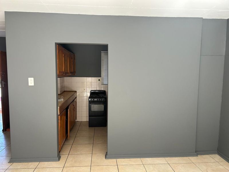 A view into a dated kitchen featuring wooden cabinetry, a tiled backsplash, and a freestanding stove, accessible from an adjacent living area.