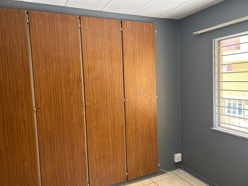 A bedroom featuring built-in wooden cupboards, tiled flooring, and a window fitted with security bars.