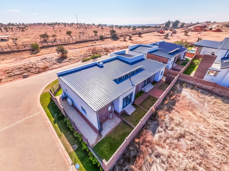 Aerial view of a modern residential property featuring a metal roof, brick boundary walls, and paved driveway in a developing estate.