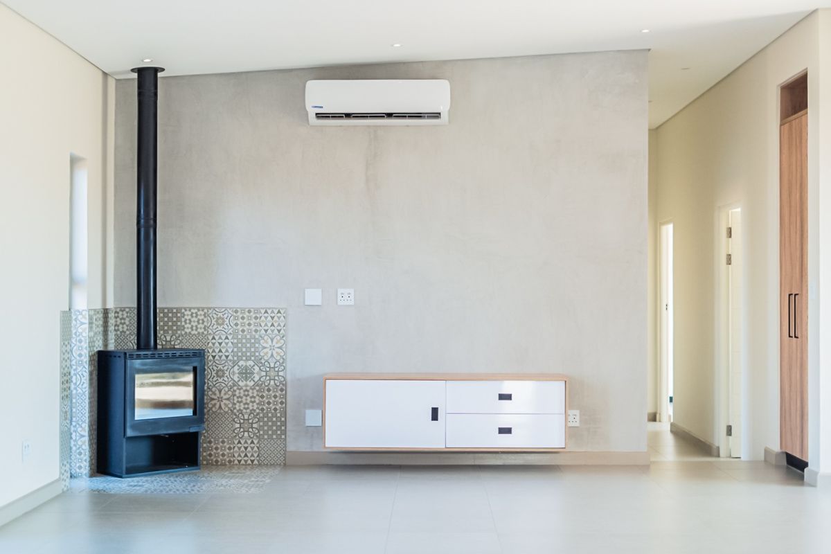 Modern living area featuring a sleek freestanding fireplace with decorative tile surround, split-system air conditioning, and neutral tiled flooring.