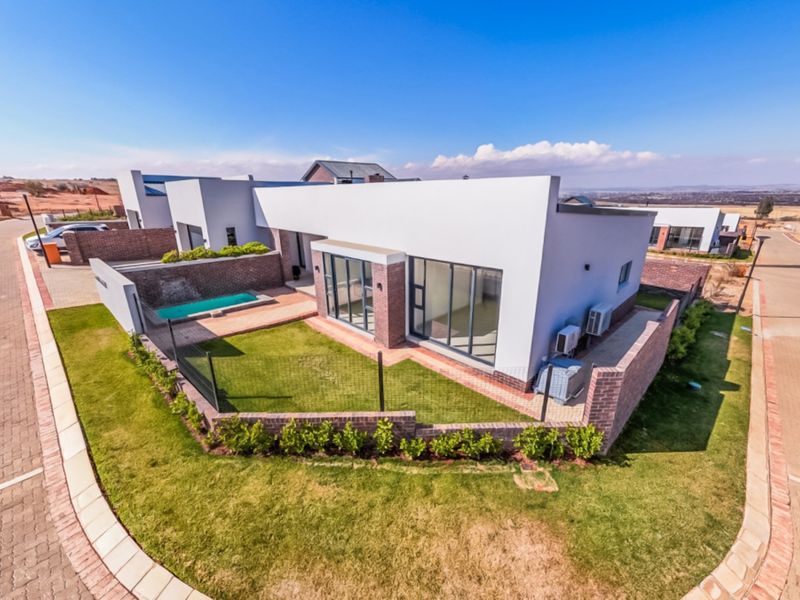 Aerial view of a modern single-story home featuring a private garden, swimming pool, paved patio area, and secure brick boundary walls.