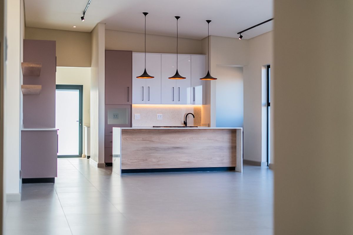 Modern kitchen featuring a central island with wood-grain finish, sleek white cabinetry, stone countertops, and contemporary pendant lighting in an open-plan layout.