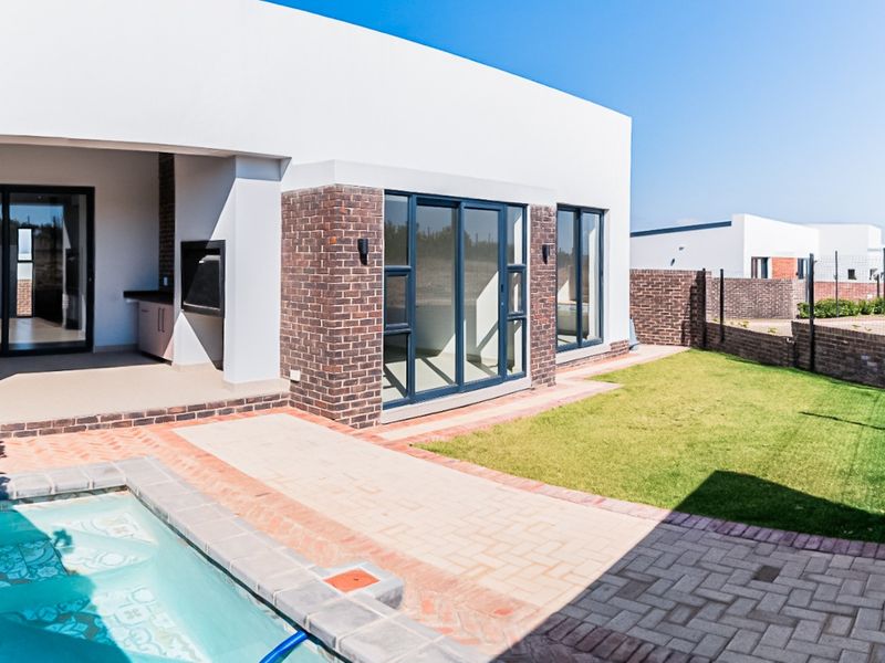 Modern rear exterior featuring a swimming pool, paved patio area with a built-in braai, and a well-maintained lawn.
