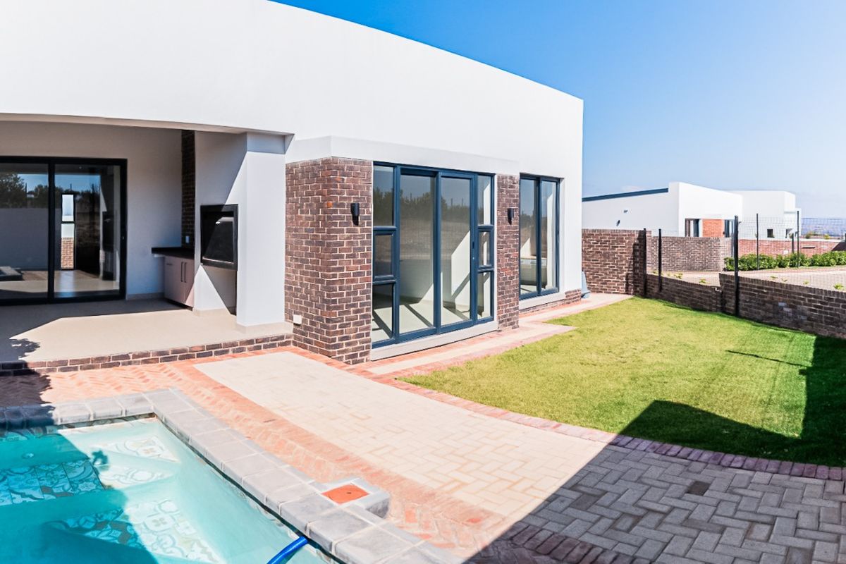 Modern rear exterior featuring a swimming pool, paved patio area with a built-in braai, and a well-maintained lawn.