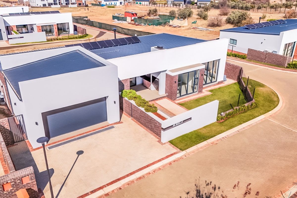 Aerial view of a modern single-story residential property featuring a double garage, solar panels, paved driveway, and a well-maintained garden.