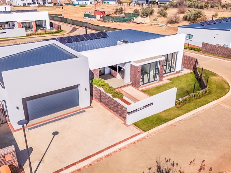 Aerial view of a modern single-story residential property featuring a double garage, solar panels, paved driveway, and a well-maintained garden.