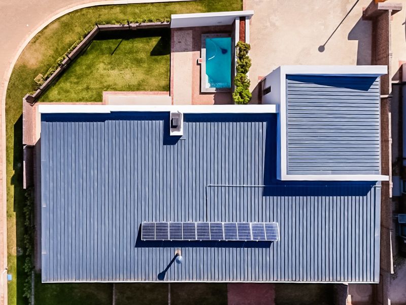 Aerial view of the property featuring a modern metal roof with integrated solar panels, a swimming pool, and a well-maintained garden.