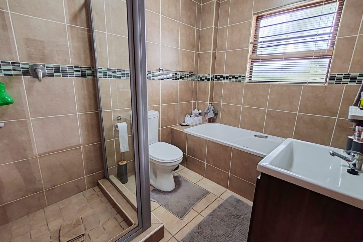 A functional bathroom featuring a glass-enclosed shower, a built-in bathtub, a toilet, and a vanity basin with neutral wall and floor tiling.