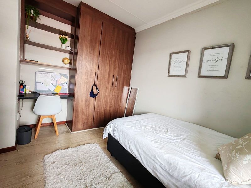 A well-maintained bedroom featuring built-in wooden cabinetry, integrated desk space with shelving, and durable laminate flooring.