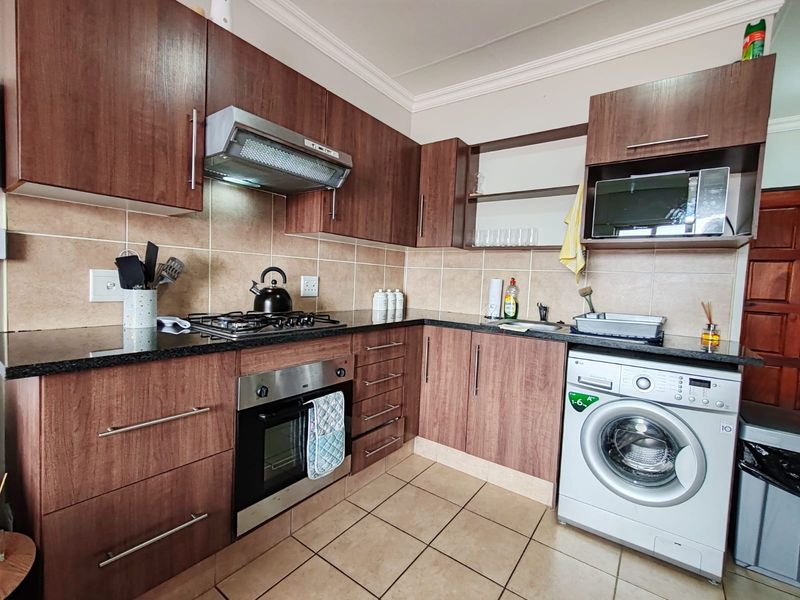A functional kitchen featuring dark wood cabinetry, granite countertops, a gas hob, built-in oven, and integrated space for a washing machine.