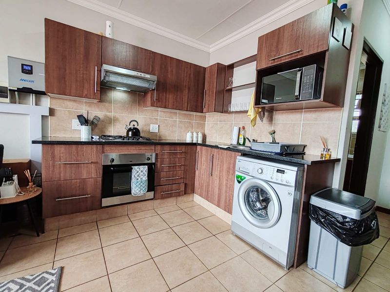 A functional kitchen featuring dark wood cabinetry, granite countertops, tiled backsplash, built-in oven, gas hob, and an integrated washing machine.