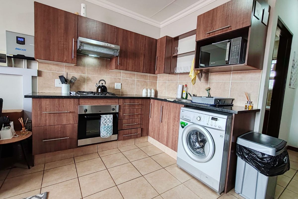 A functional kitchen featuring dark wood cabinetry, granite countertops, tiled backsplash, built-in oven, gas hob, and an integrated washing machine.
