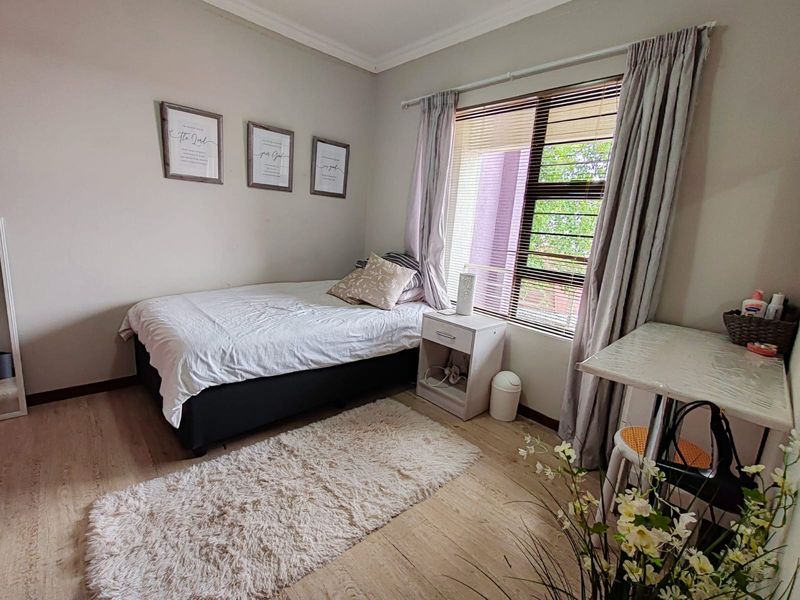 A well-lit bedroom featuring light-toned laminate flooring, neutral wall finishes, and a window fitted with blinds and curtains.