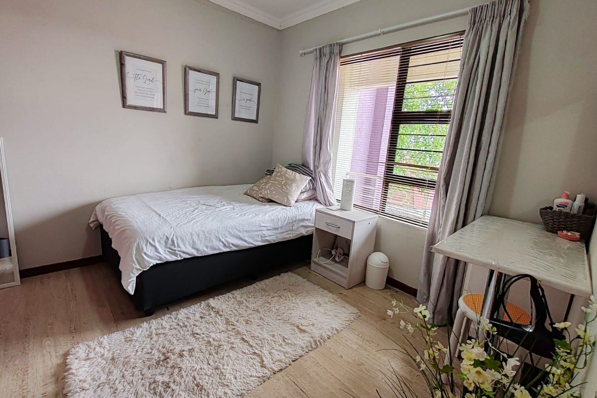 A well-lit bedroom featuring light-toned laminate flooring, neutral wall finishes, and a window fitted with blinds and curtains.