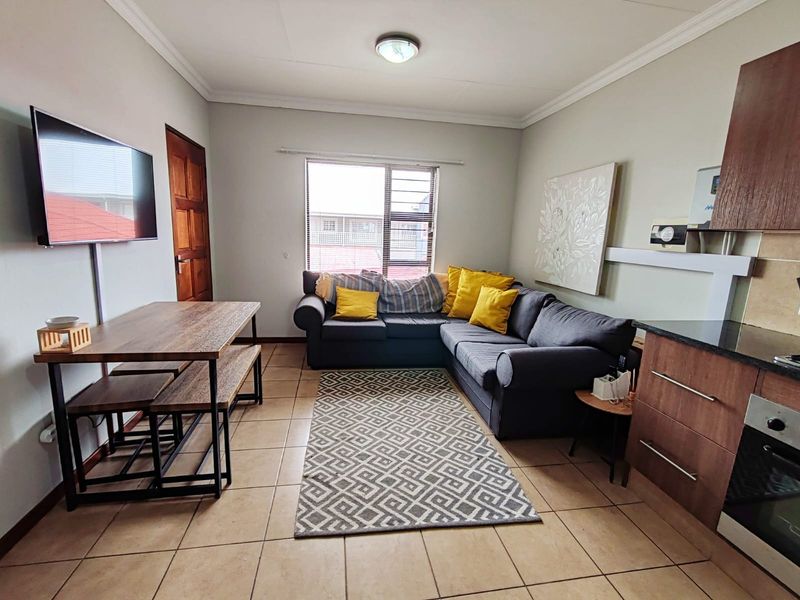 Open-plan living area featuring tiled floors, a compact kitchen with built-in oven and cabinetry, and a window with security bars.