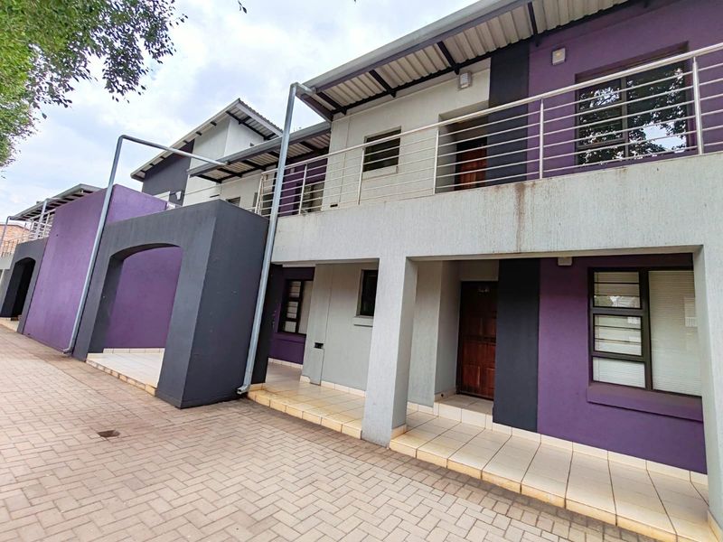 Front elevation of a multi-story apartment complex featuring a paved entrance, tiled patio areas, and a modern balcony with stainless steel railings.