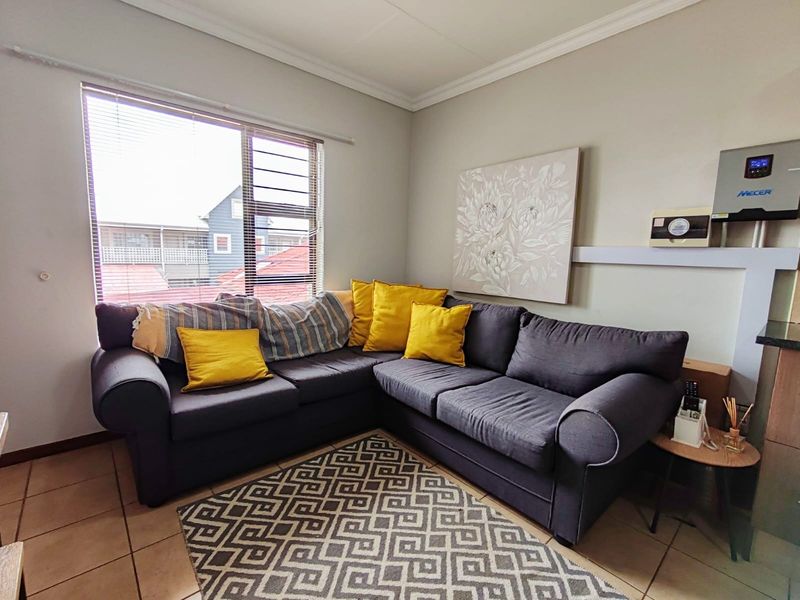A living room featuring tiled flooring, a window with security bars, and a wall-mounted inverter system.