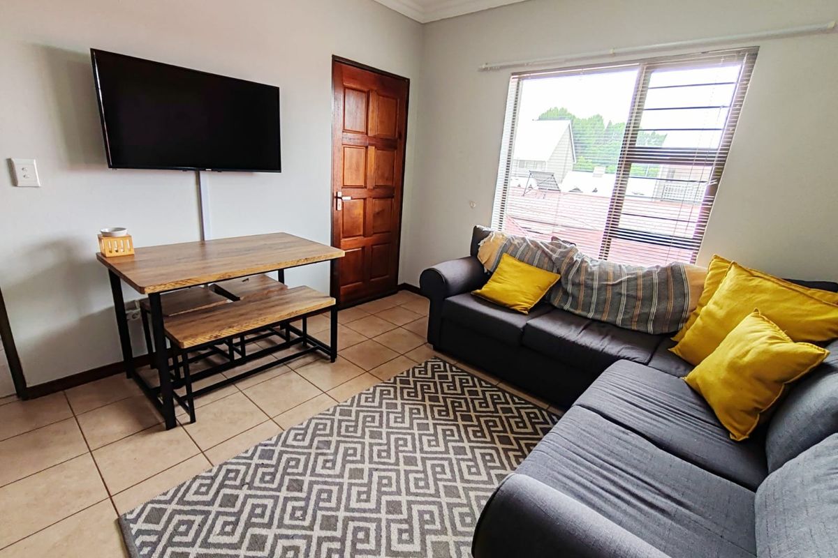 A functional living room featuring tiled flooring, a timber door, and a window fitted with security bars, providing a practical and well-lit living space.
