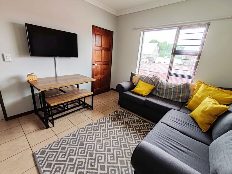 A functional living room featuring tiled flooring, a timber door, and a window fitted with security bars, providing a practical and well-lit living space.
