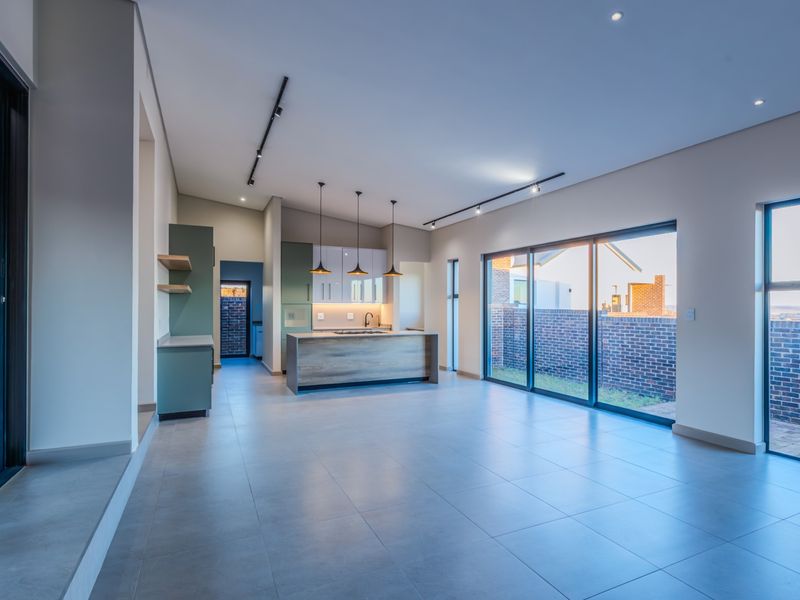 Modern open-plan living and kitchen area featuring sleek cabinetry, a central island, tiled floors, and large sliding doors opening to the rear garden.
