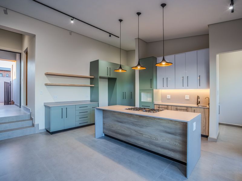 Modern kitchen featuring a central island with gas cooktop, two-tone cabinetry, floating shelves, and contemporary pendant lighting in an open-plan layout.