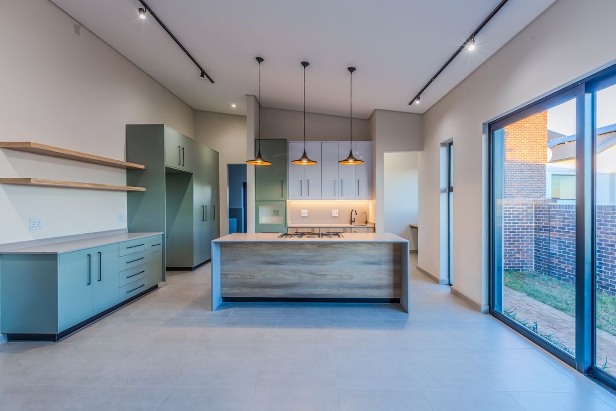 Modern kitchen featuring a central island with gas cooktop, sleek cabinetry, stone countertops, and large sliding glass doors opening to the rear garden.