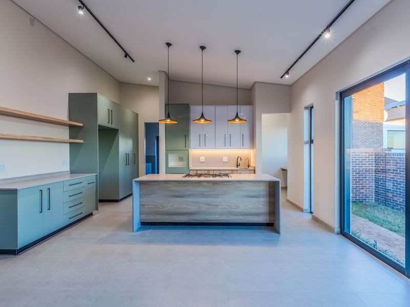 Modern kitchen featuring a central island with gas cooktop, sleek cabinetry, stone countertops, and large sliding glass doors opening to the rear garden.