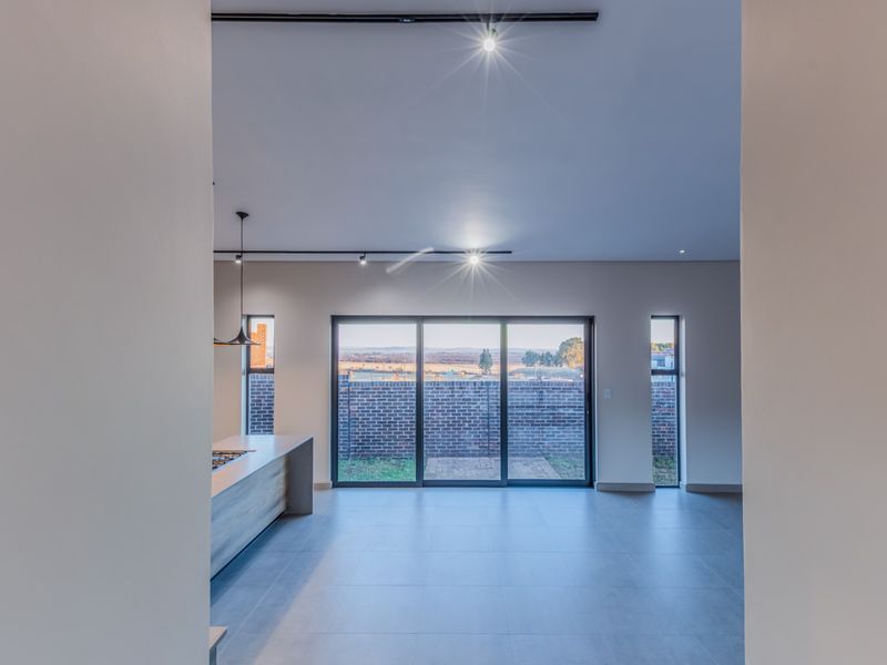 Modern open-plan living area featuring a sleek kitchen island with built-in hob, large sliding glass doors, and contemporary track lighting.