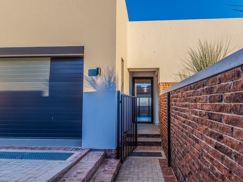 Modern front entrance featuring a sleek garage door, brick boundary wall, and paved walkway leading to the main entry.