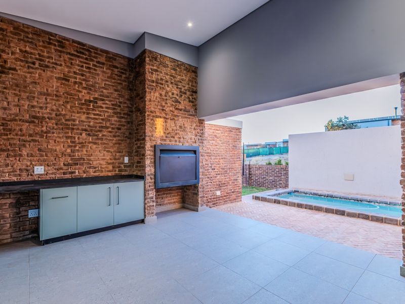 Covered patio area featuring exposed brick walls, built-in braai, cabinetry, and direct access to a private swimming pool.