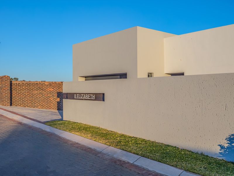 Modern exterior front facade featuring a clean rendered boundary wall, paved driveway, and contemporary street-facing address signage.