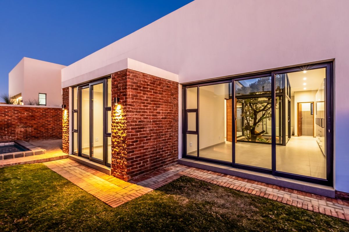 Modern rear elevation featuring exposed brickwork, large sliding glass doors, and a central internal courtyard, illuminated by warm exterior lighting.