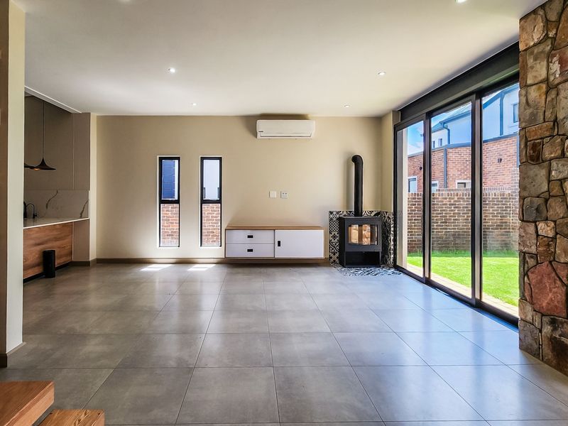 Spacious open-plan living area featuring large sliding doors to the garden, a stone feature wall, wood-burning fireplace, and modern tiled flooring.