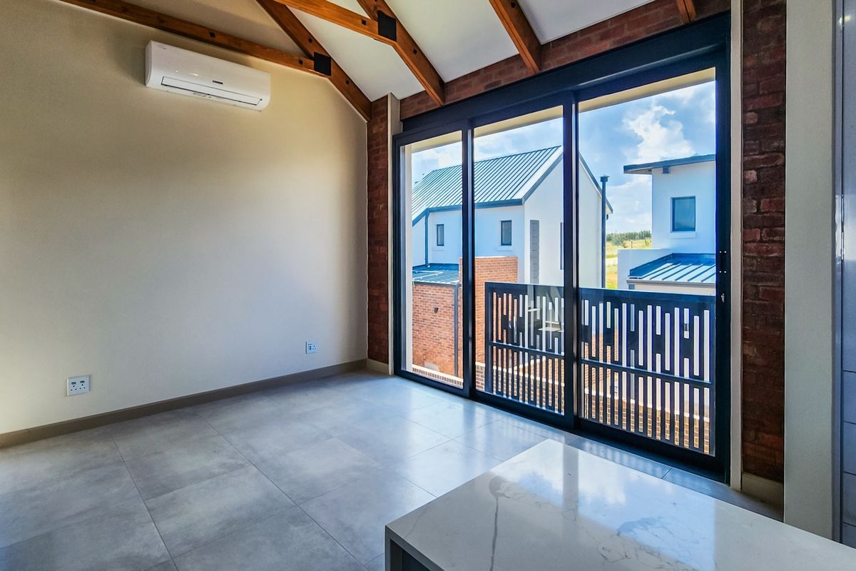Bright bedroom featuring exposed timber rafters, brick accent wall, tiled flooring, and large sliding glass doors opening to a private balcony.
