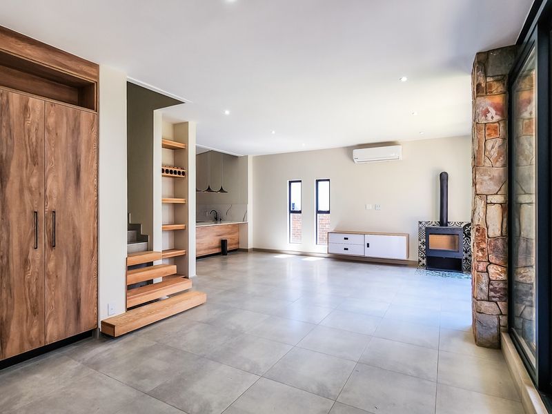 Spacious open-plan living area featuring modern tiled floors, a stone feature wall, a built-in fireplace, and integrated wooden cabinetry with a staircase.