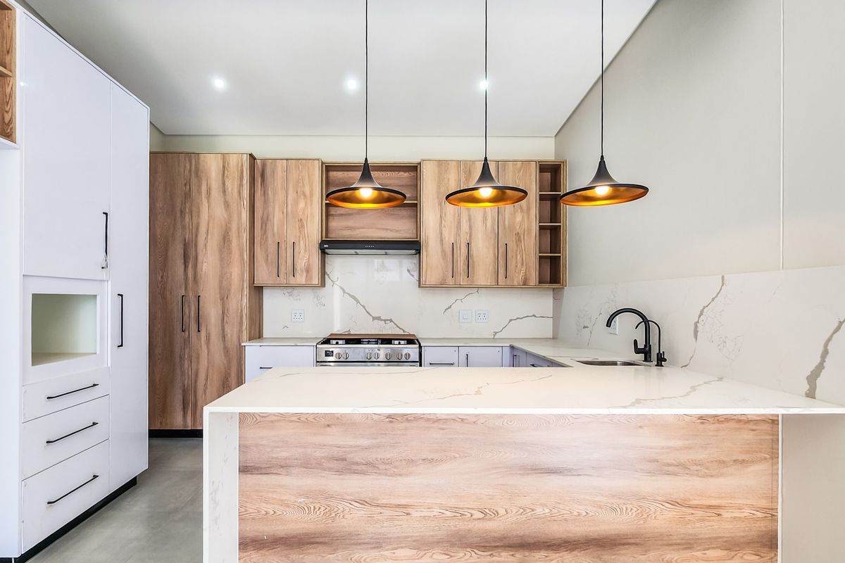 Modern kitchen featuring wood-grain cabinetry, stone countertops with marble-look backsplash, integrated gas stove, and stylish pendant lighting.
