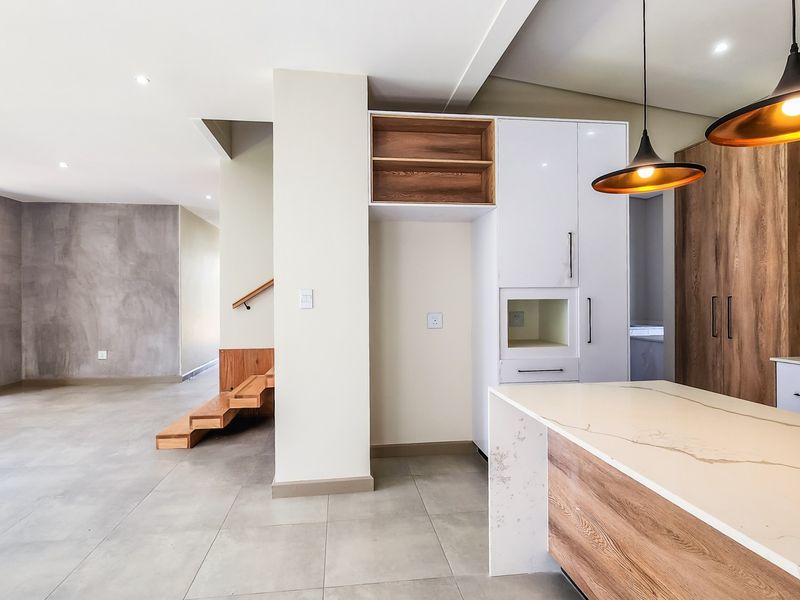 Modern open-plan living area featuring a sleek kitchen with stone island, built-in cabinetry, and seamless transition to the adjacent living space and staircase.