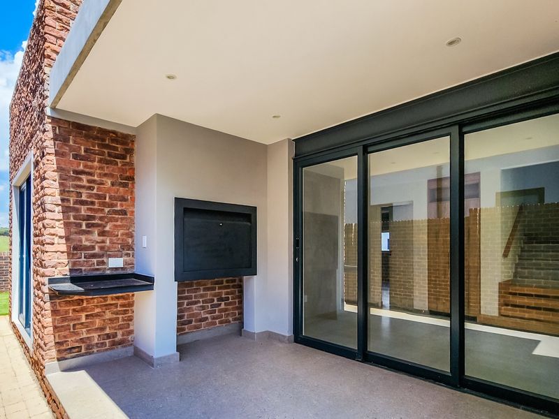 A modern covered patio featuring exposed brick and stone cladding, a built-in braai, and large sliding glass doors leading into the home.