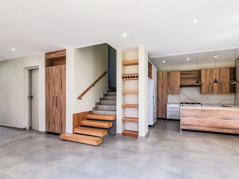 Modern open-plan living area featuring a sleek kitchen with wood-finish cabinetry, stone backsplash, and a floating wooden staircase.