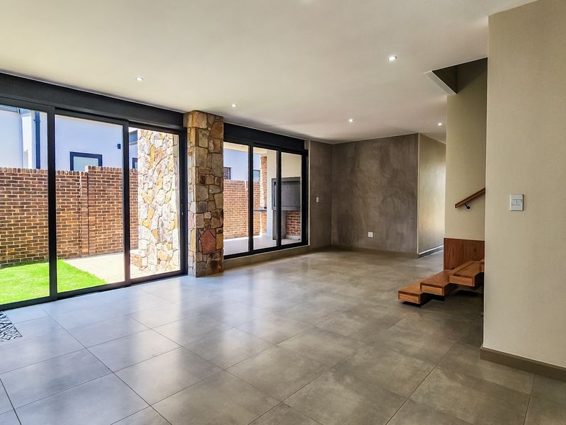 Spacious open-plan living area featuring large format floor tiles, a striking stone-clad pillar, and a modern floating timber staircase with seamless access to the garden.