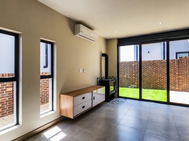 Modern living room featuring tiled floors, a sleek fireplace, air conditioning, and large sliding doors opening to a private garden area.