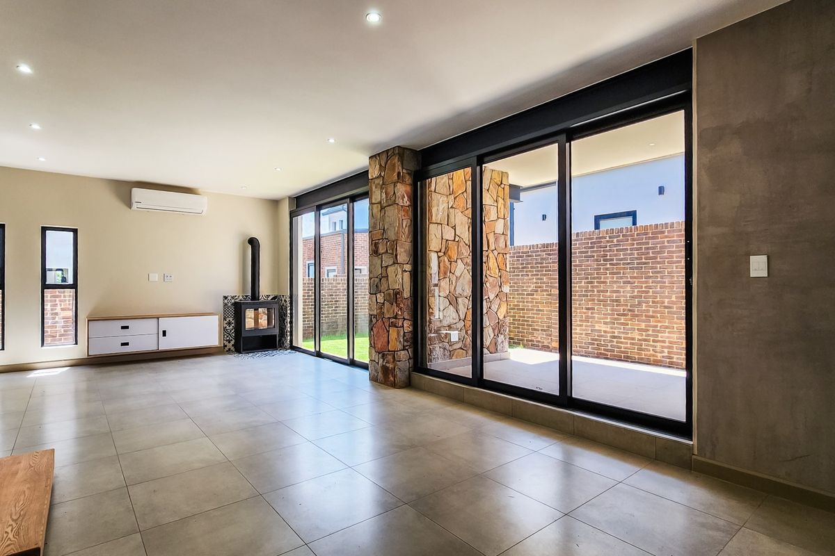 Spacious living area featuring large aluminium sliding doors, a stone-clad pillar, a modern fireplace, and sleek tiled flooring with recessed lighting.