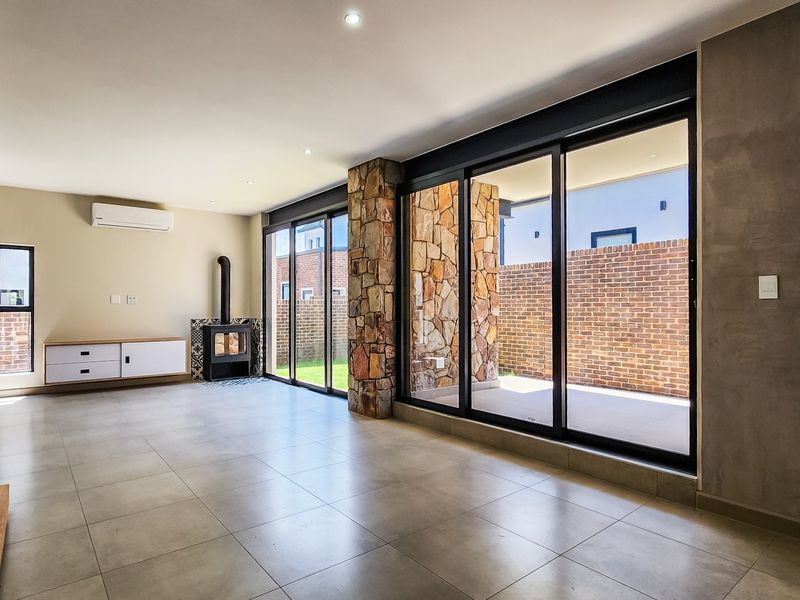 Spacious living area featuring large aluminium sliding doors, a stone-clad pillar, a modern fireplace, and sleek tiled flooring with recessed lighting.