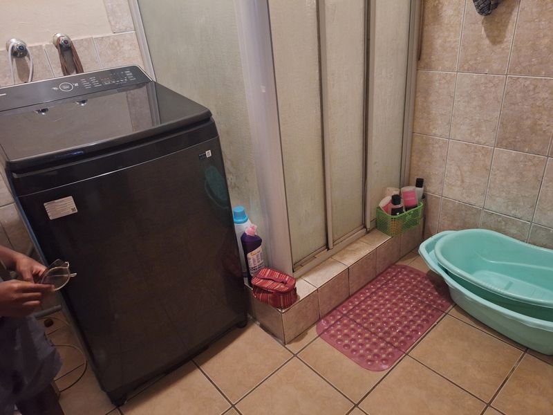 A functional bathroom featuring a shower enclosure with tiled walls and flooring, currently accommodating a washing machine.
